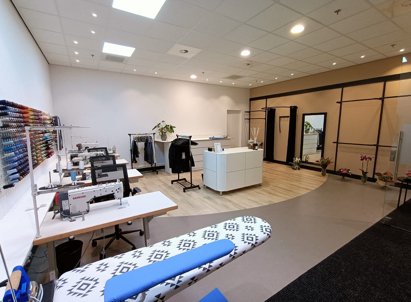 Het atelier van Kledingreparatie & Stomerij Koningshoek: naaimachines, de wand met garen, strijkplank en paskamers