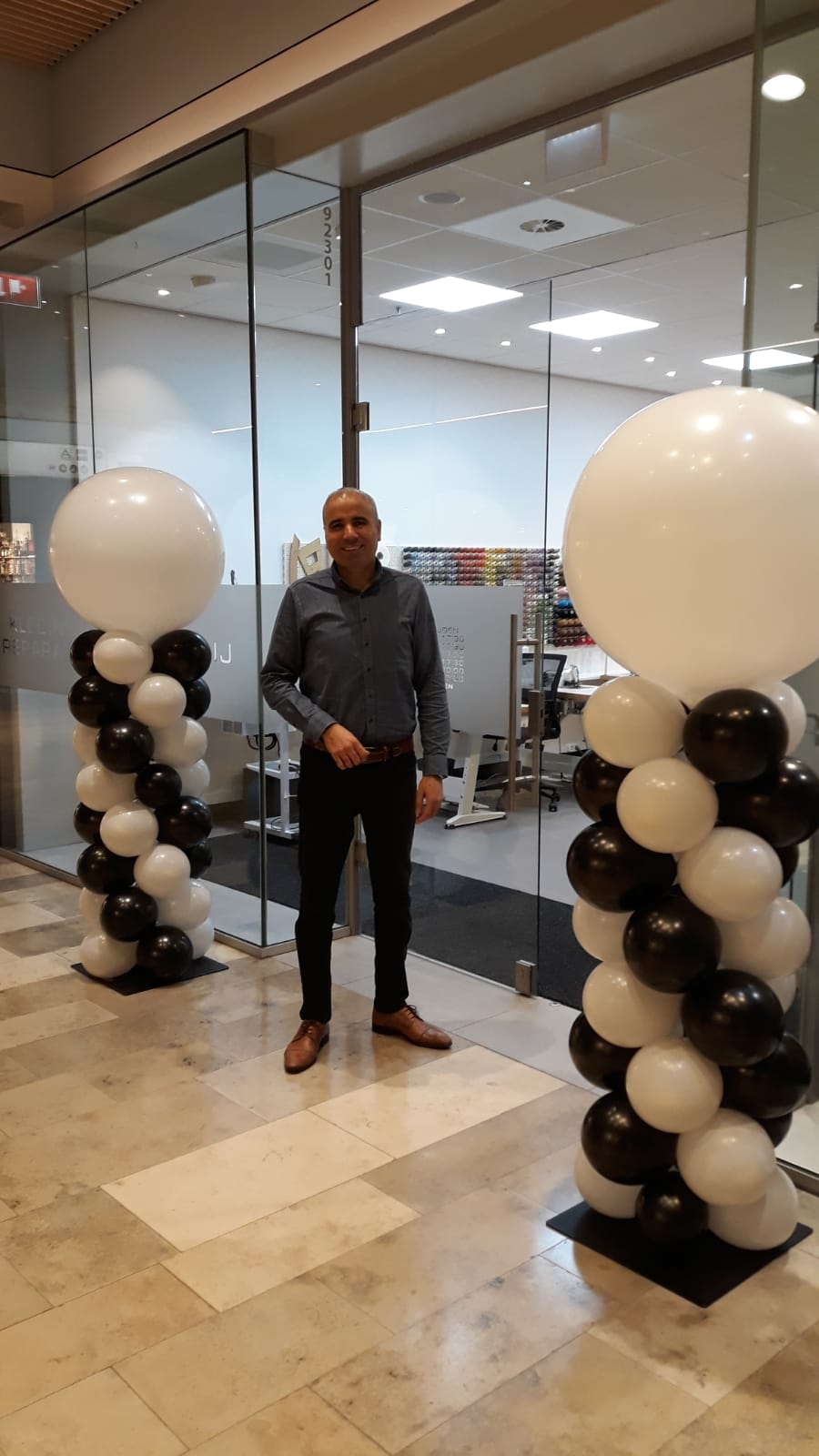Selam Demir voor de glazen ingang van de winkel in Koningshoek, met ballonnen aan weerszijden van de deur