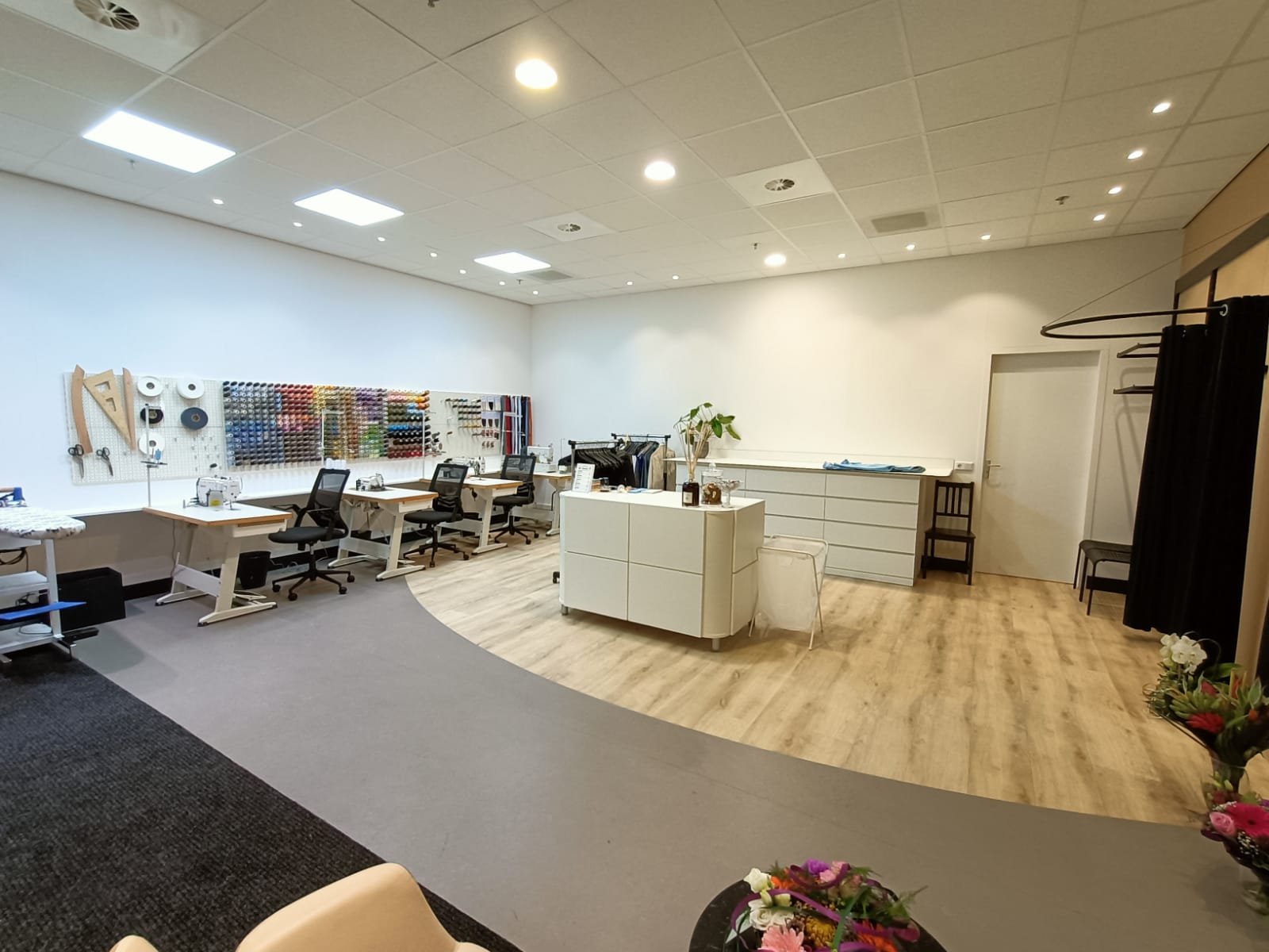 De werkplekken in het atelier met naaimachines, de balie en de paskamer