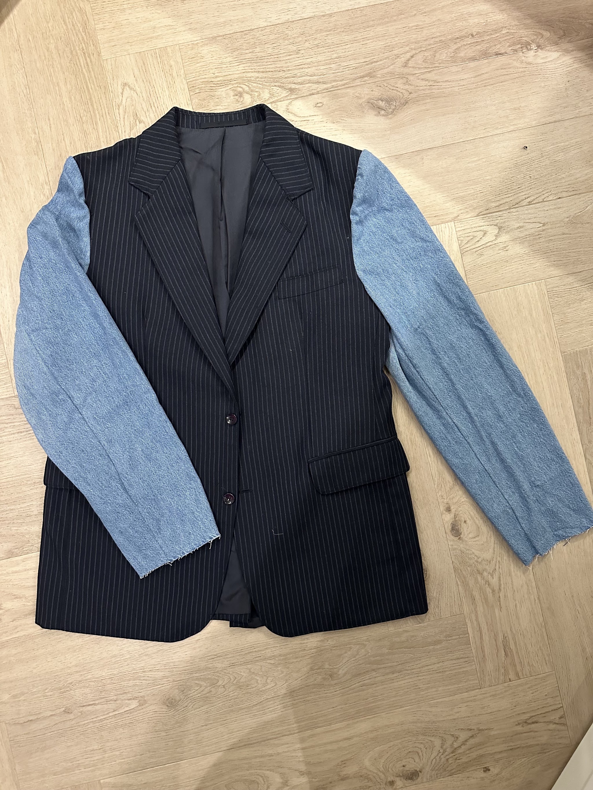 Krijtstreepcolbert met lichtblauwe denim mouwen, plat neergelegd op een houten vloer